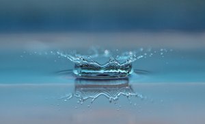 Das Bild zeigt einen zerplatzenden Wassertropen auf einer Wasseroberfläche