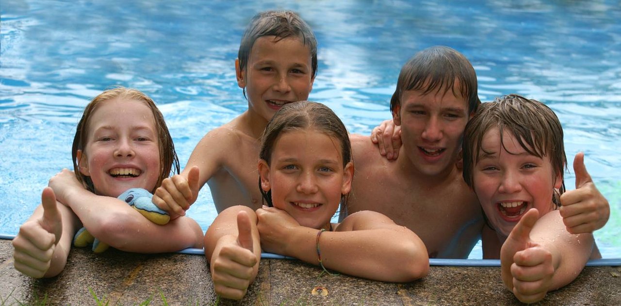 Das Bild zeigt fünf Kinder am Rand eines Schwimmbeckens, die freundlich ihre Daumen in die Höhe recken.