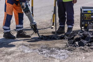 Das Foto zeigt die Unterkörper von zwei Bauarbeitern. Einer stemmt mit dem Presslufthammer eine Straße auf.