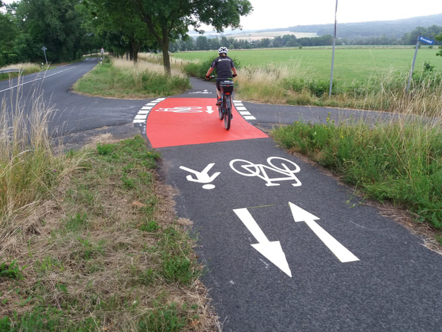 Radfahrer auf roter Radwegmarkierung bei Einmündung in Radweg